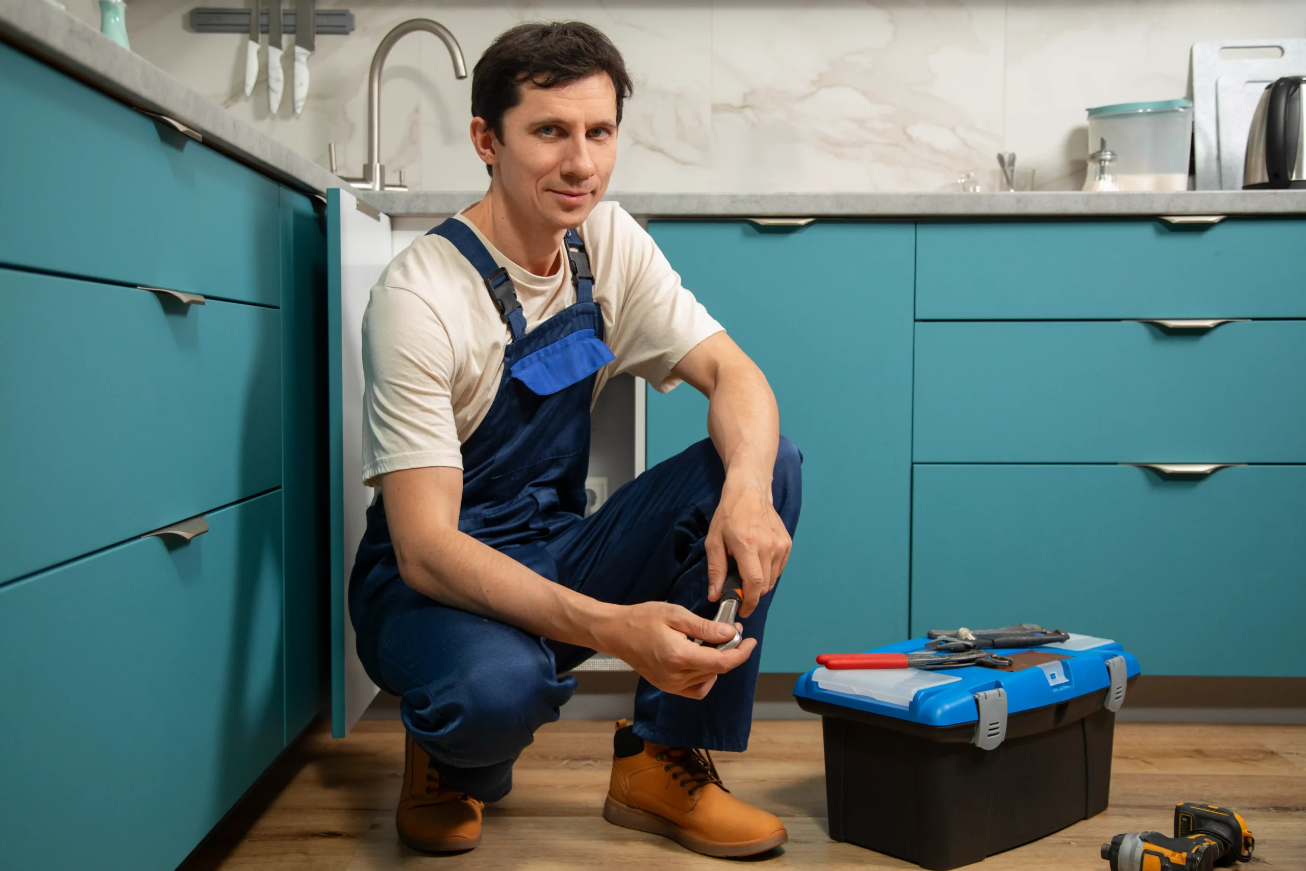 Plombier Liège accroupi dans une cuisine moderne avec sa boîte à outils